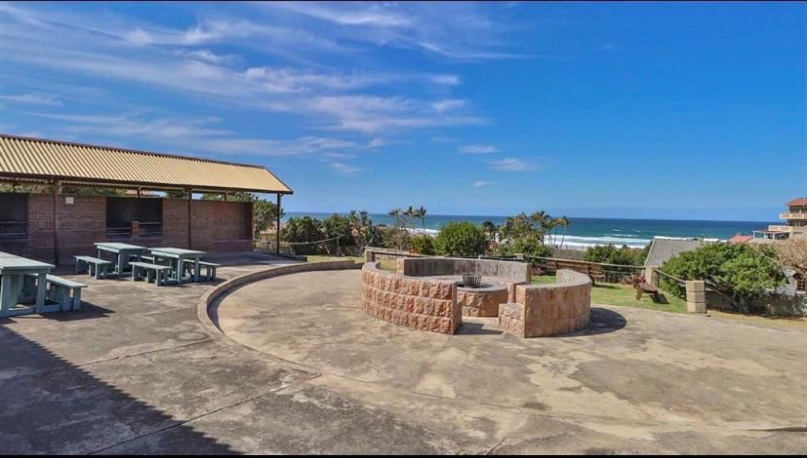 Tetelestai Recovery Centre outdoor boma and braai area with picnic benches, a thatch-roofed shelter, and an open ocean view — not a secured prison environment